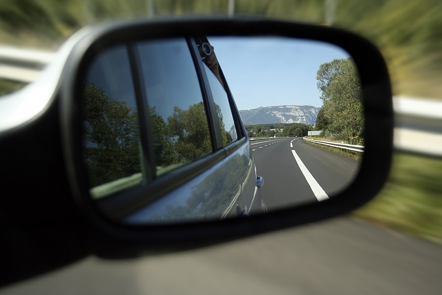 Car side-view mirror looking back on a highway